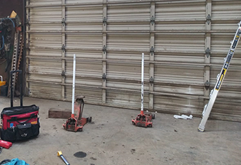 Large sectional steel garage door undergoing routine maintenance in a Burr Ridge, IL workshop, tools and ladder