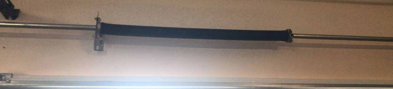 Close-up view of a newly replaced black torsion garage door spring installed above a residential garage door in Westmont, IL